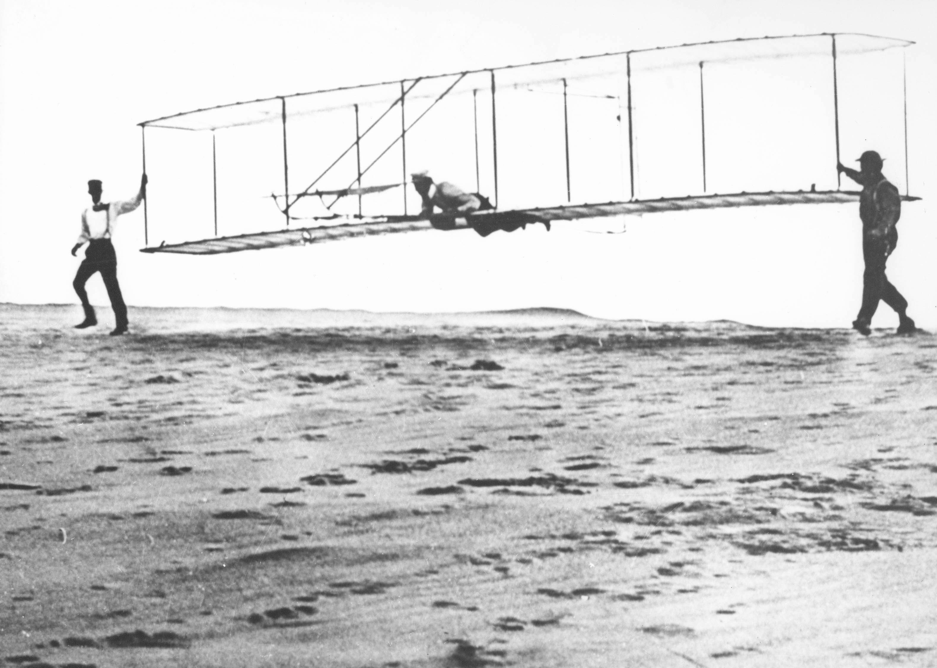 Historic photo of the Wright brothers’ third test glider being launched at Kill Devil Hills, North Carolina, on October 10, 1902. Wilbur Wright is at the controls, Orville Wright is at left, and Dan Tate (a local resident and friend of the Wright brothers) is at right.